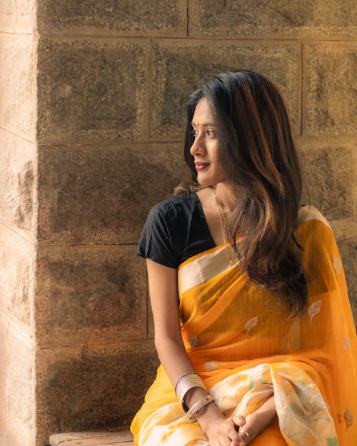 A woman in a yellow sari sitting on a stone wall
