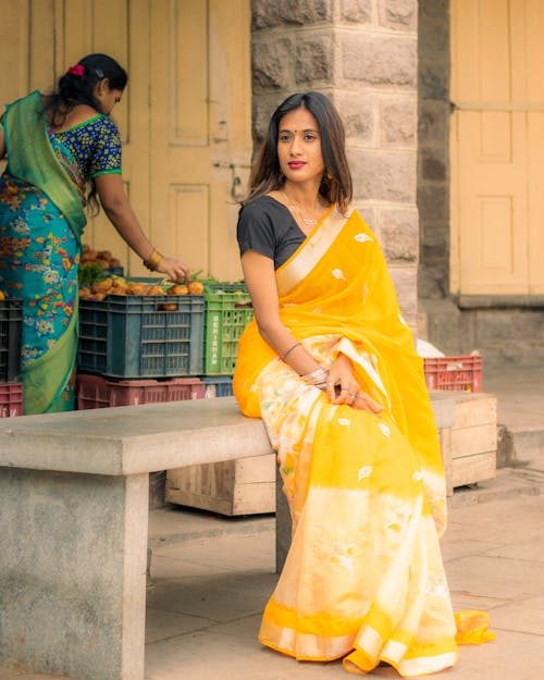 A woman in a yellow sari sitting on a bench