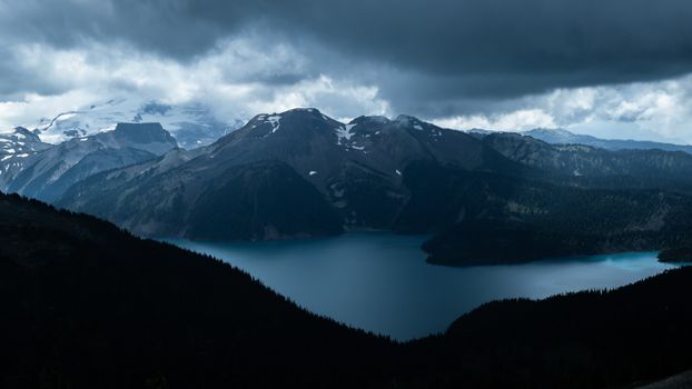 A breathtaking aerial view of Garibaldi Lake surrounded by rugged mountains under dramatic clouds in Garibaldi, BC, Canada.