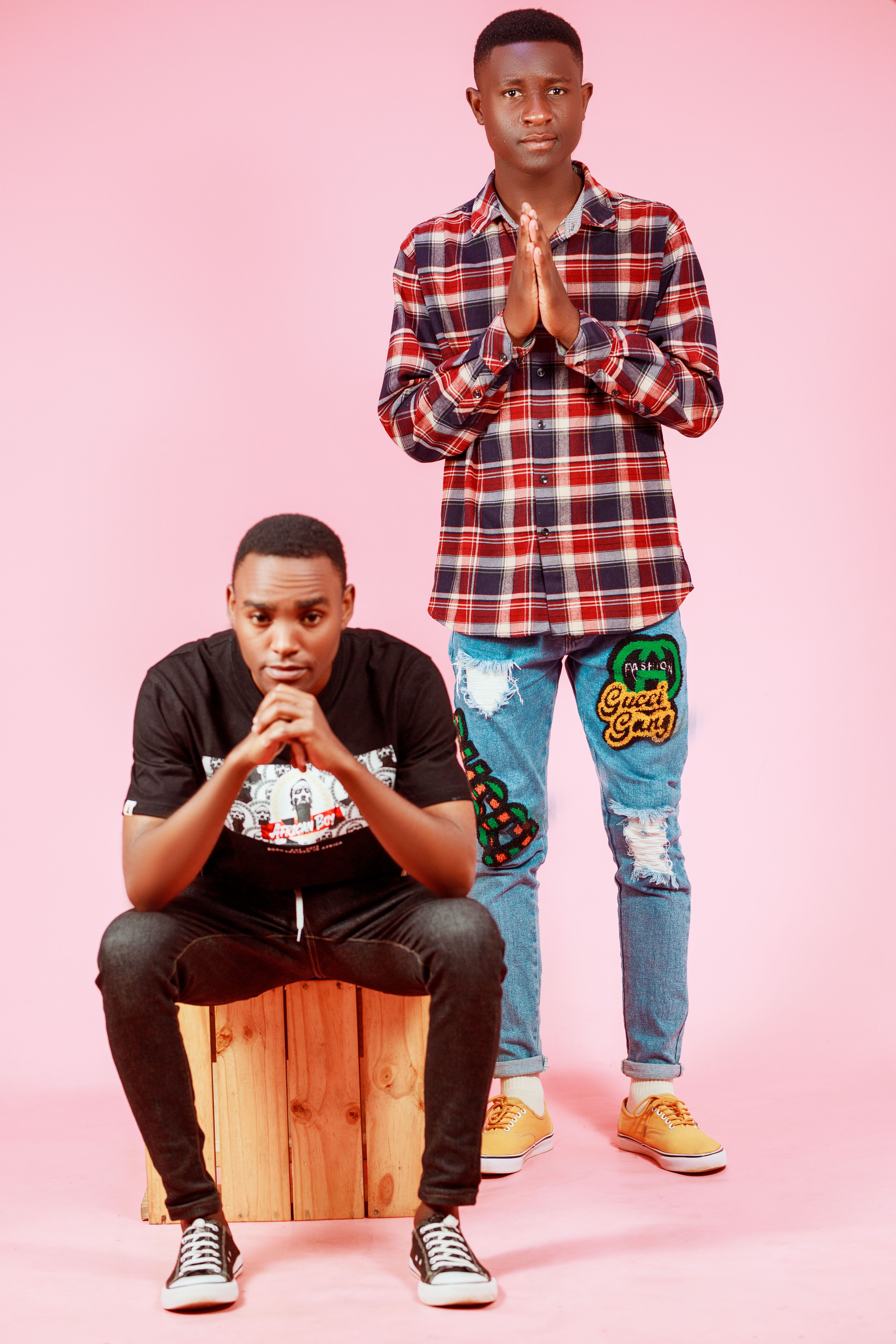 Stylish portrait of two young men posing against a pink backdrop.