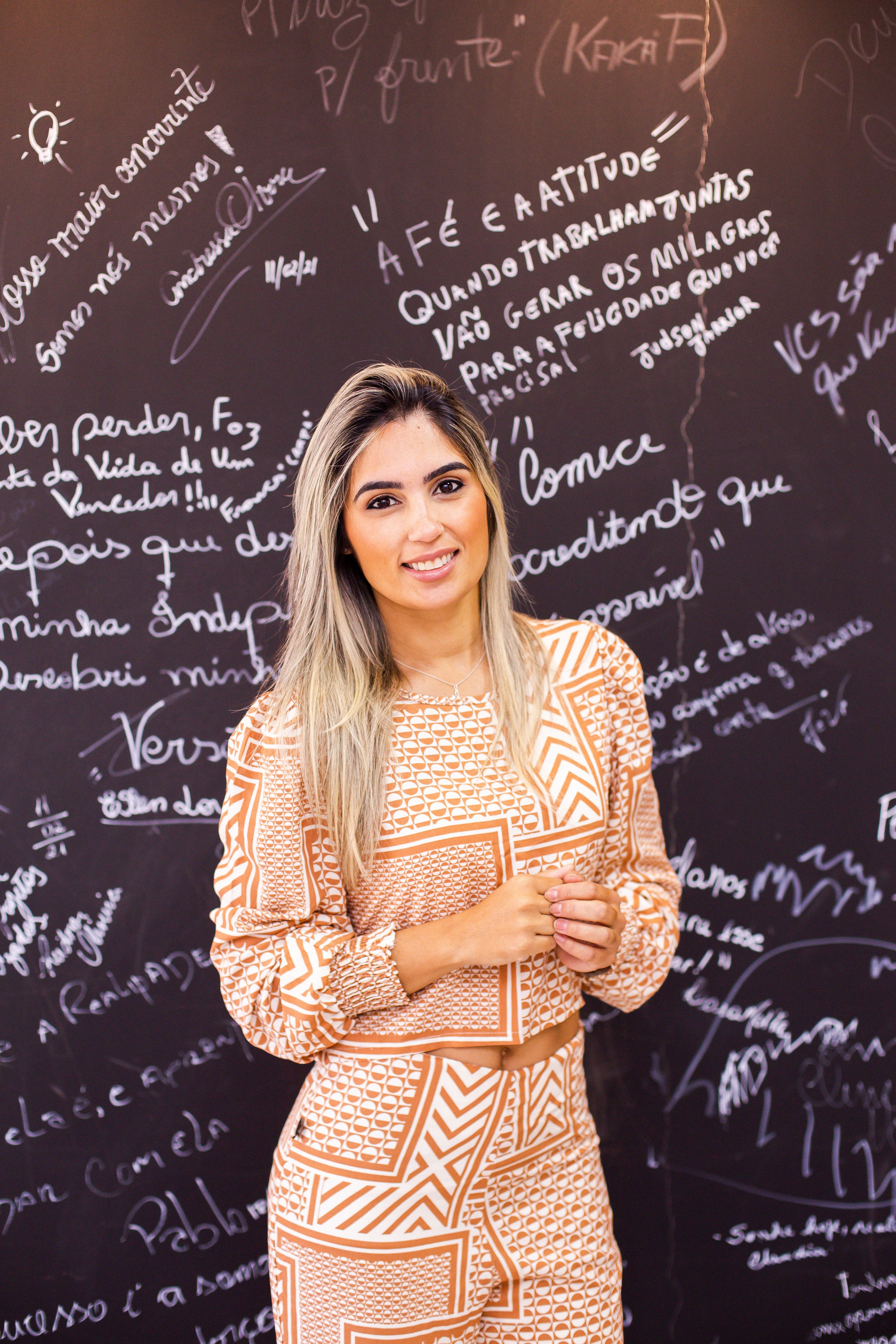 Portrait of a smiling woman standing against a chalkboard with writings, in a fashionable patterned outfit.