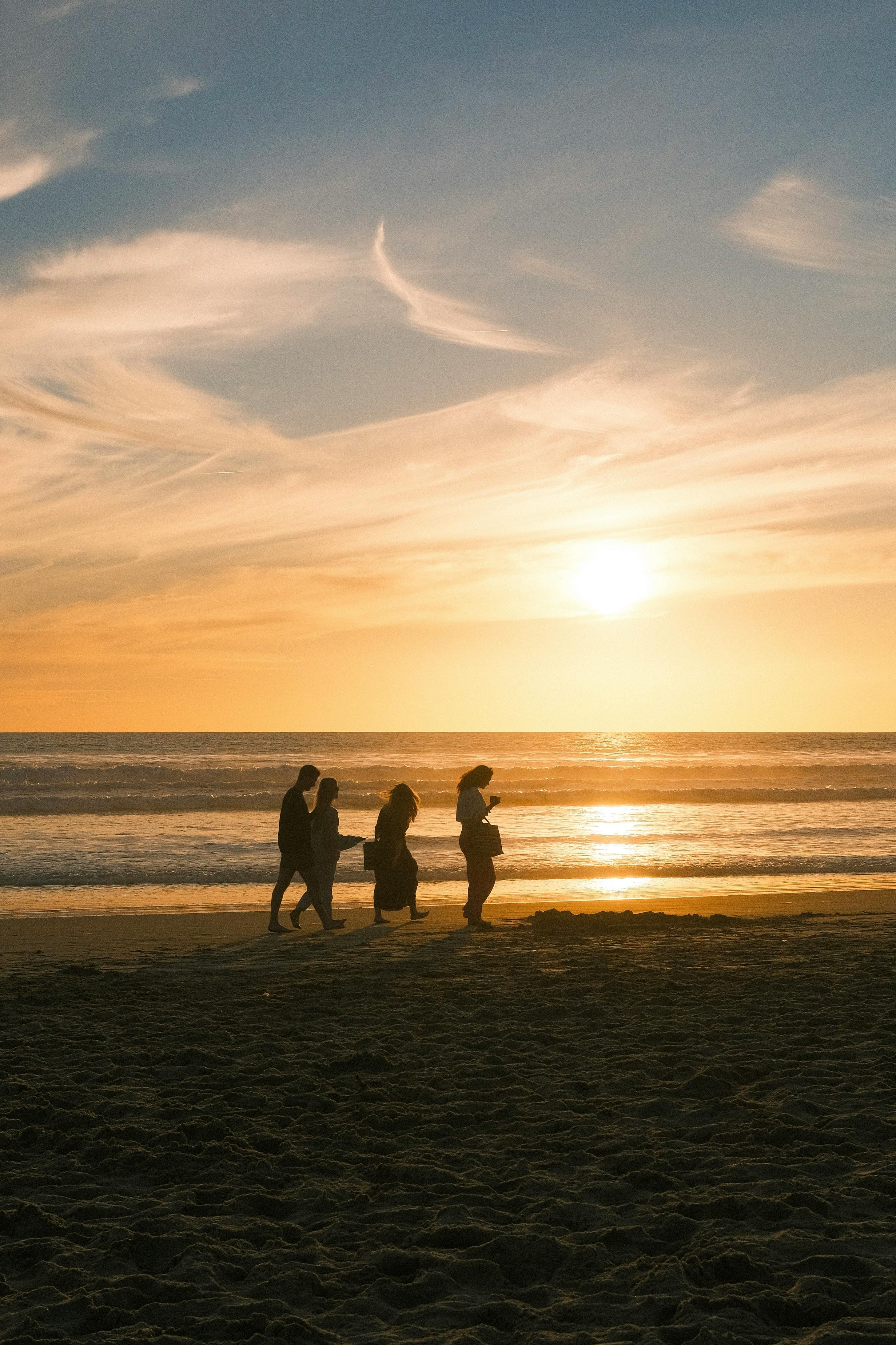 A group enjoys a peaceful walk at Costa da Caparica beach during a stunning sunset, Portugal.