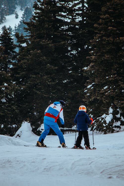 A man and a child are skiing down a snowy slope