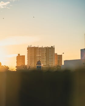Silhouette of urban buildings against a sunrise backdrop with a clear sky.