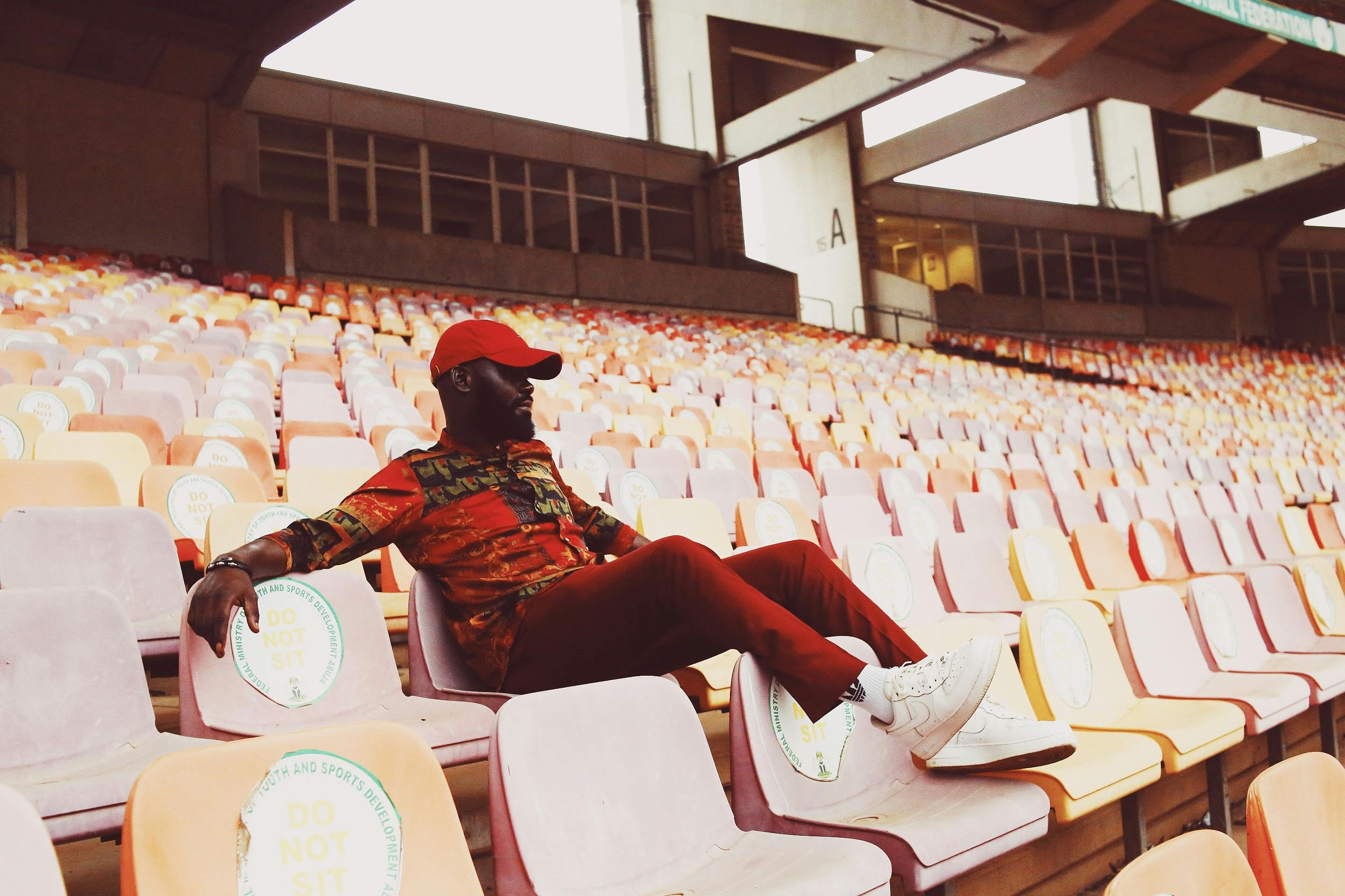 A fashionable man in a red cap relaxes in a colorful stadium, embodying urban style and leisure.