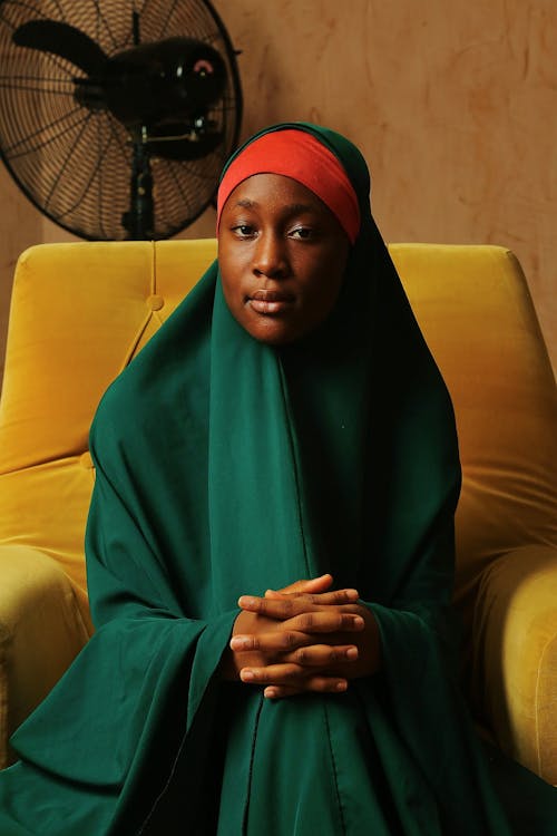 Young Woman Sitting in an Armchair in Traditional Clothing and a Hijab 