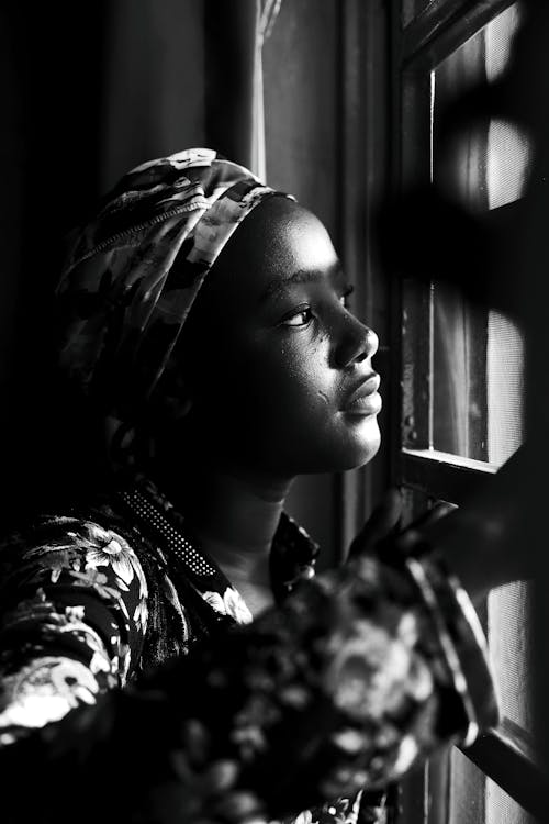 A black and white photo of a woman looking out a window