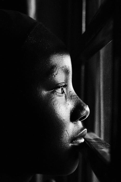 A black and white photo of a young girl looking out a window