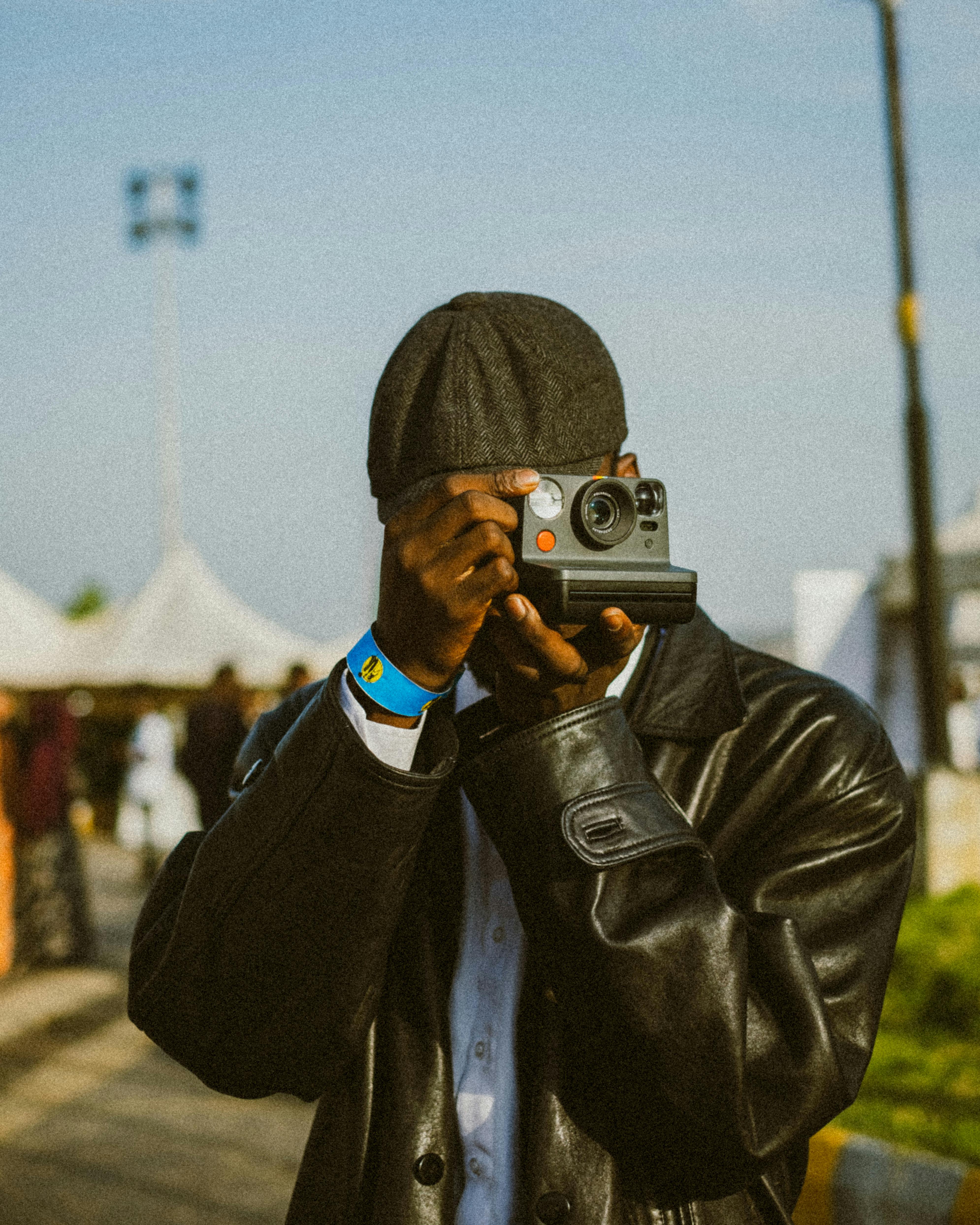 A black man in a leather jacket uses a Polaroid camera. Capturing urban moments outdoors.