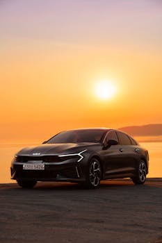 Stylish gray Kia sedan silhouetted against a vibrant sunset over the ocean.