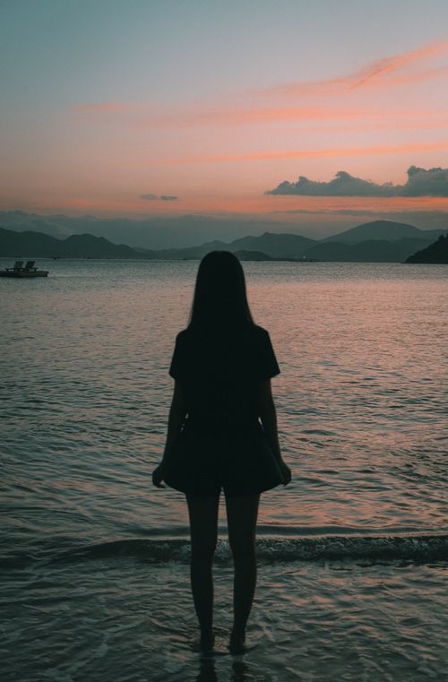 Free A woman stands by the sea during dusk, silhouetted against a beautiful twilight sky. Stock Photo