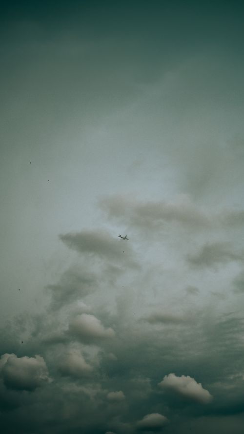 Free A distant airplane flying amidst dramatic clouds, portraying freedom and adventure. Stock Photo