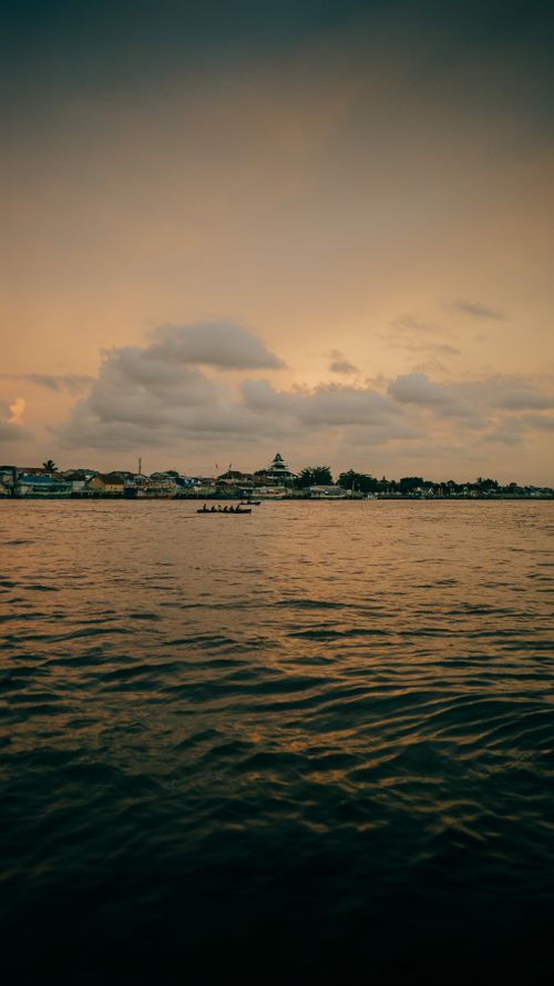Free A tranquil view of a city skyline at sunset with a rowboat on the calm sea. Stock Photo