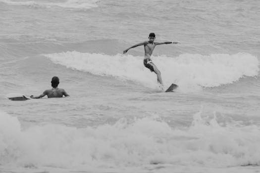 A black and white photo capturing two surfers riding waves at Canoa Quebrada beach.