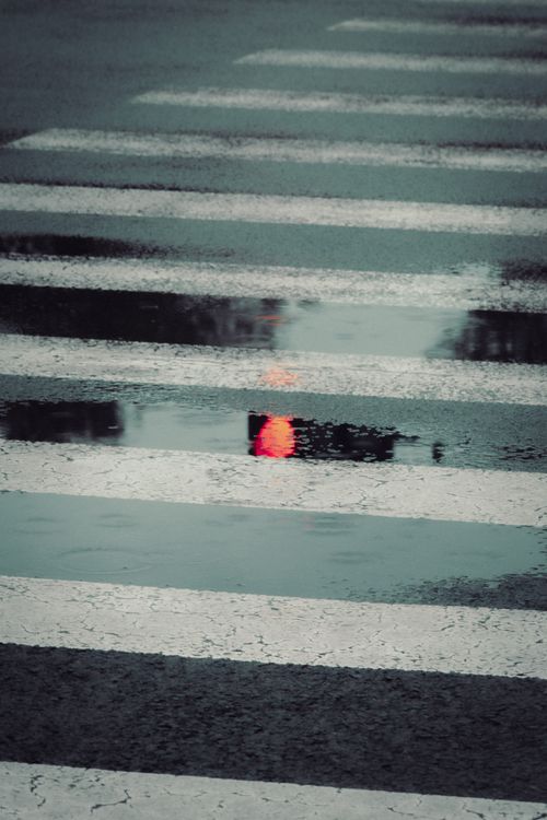 Free A rainy city street with a traffic light reflected in a puddle on a crosswalk. Stock Photo