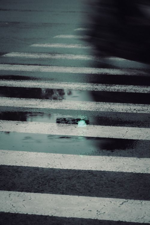 Free A moody urban crosswalk with raindrops reflecting traffic lights in puddles. Stock Photo