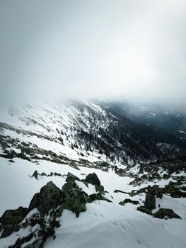 Breathtaking view of snowy mountains with fog and rocks in winter serenity.