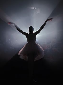 A silhouette of a ballerina with arms gracefully raised against dramatic lighting, conveying elegance.