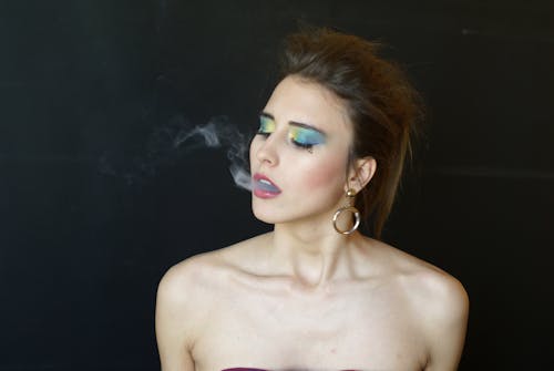 A woman with colorful makeup and a cigarette