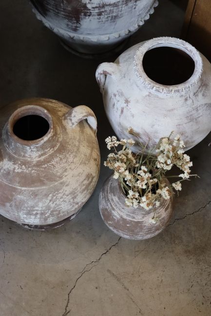 Set of rustic clay vases with dried flowers from an overhead perspective on a textured surface.