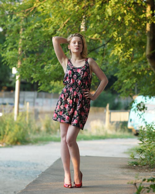 A woman in a floral dress and red heels standing on a sidewalk