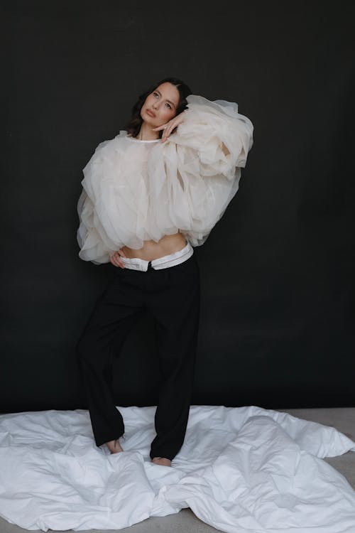 A woman in a white top and pants posing on a bed