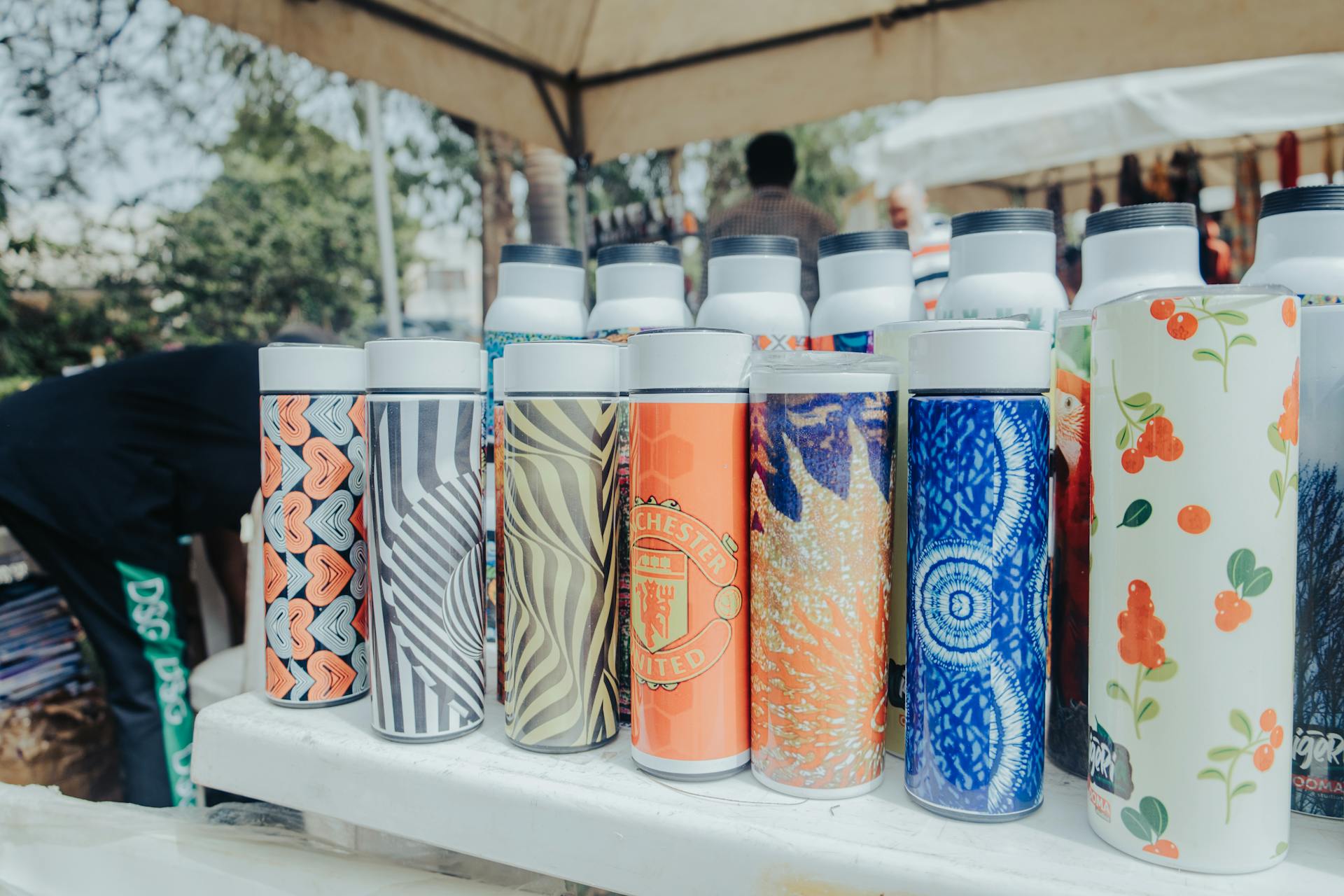 Vibrant insulated bottles showcased at an outdoor market in Abuja, Nigeria.
