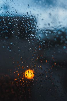 Blurred view of evening lights through a rain-soaked window pane, evoking a calm mood.