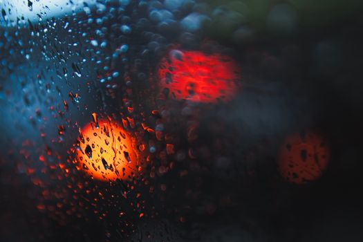Close-up of raindrops on a window with blurred lights creating a moody ambiance.