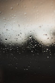 Close-up of raindrops on a windowpane with blurred outdoor evening scene.