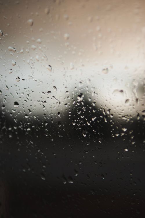 Free Close-up of raindrops on a windowpane with blurred outdoor evening scene. Stock Photo