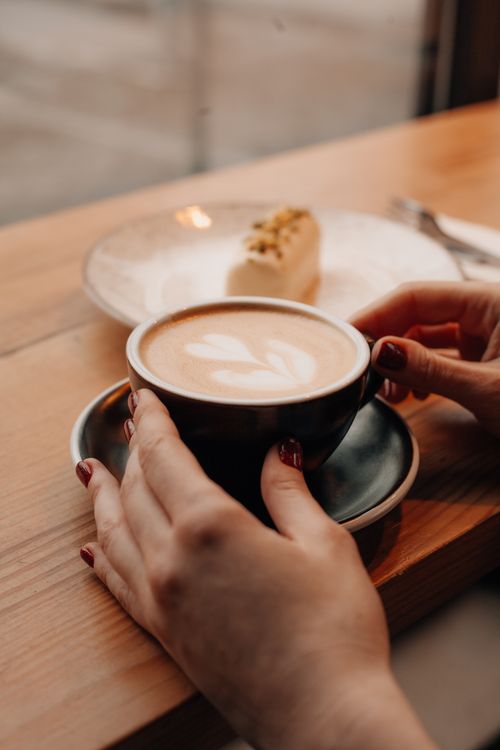 Free Hands holding a cappuccino with frothy latte art in a warm, inviting setting. Stock Photo
