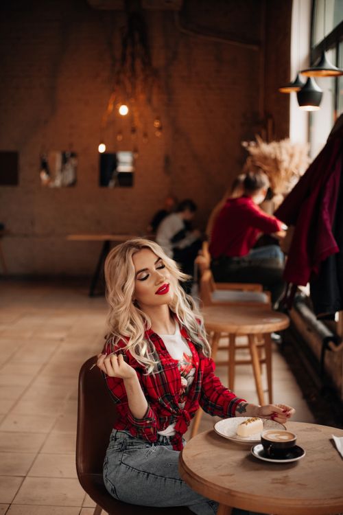 Free Blonde woman in red plaid shirt enjoying coffee and cake in a warm café. Stock Photo