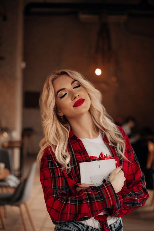 Free Fashionable blonde woman with red lipstick holding a book indoors, eyes closed in peaceful expression. Stock Photo