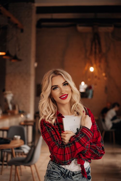 Free Portrait of a blonde woman smiling indoors holding a notebook in a cozy cafe environment. Stock Photo