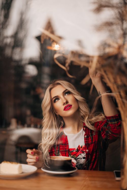 Free Blonde woman sitting in a café, gazing outside the window while enjoying coffee and cake. Stock Photo