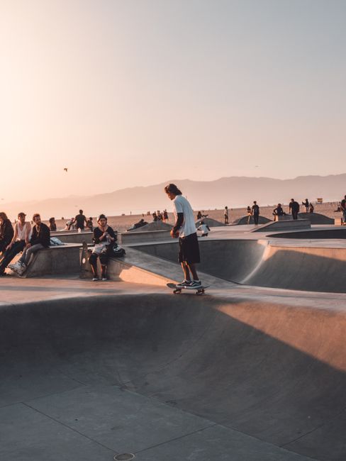 Skateboarders perform tricks at Venice Skate Park with a vibrant sunset in Los Angeles.