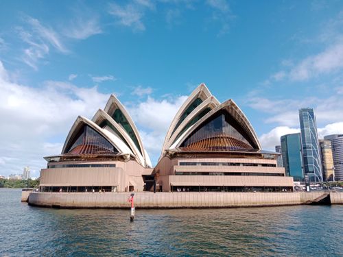 Free Iconic Sydney Opera House with skyscrapers in the city's skyline under a bright blue sky. Stock Photo