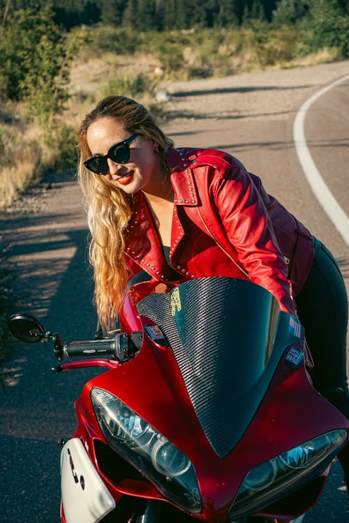 A woman in a red leather jacket posing on a motorcycle