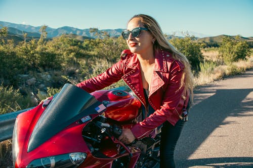 A woman in a leather jacket is sitting on a red motorcycle