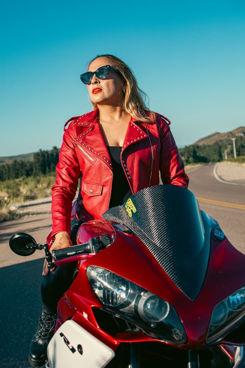 A woman in sunglasses and a red leather jacket on a motorcycle