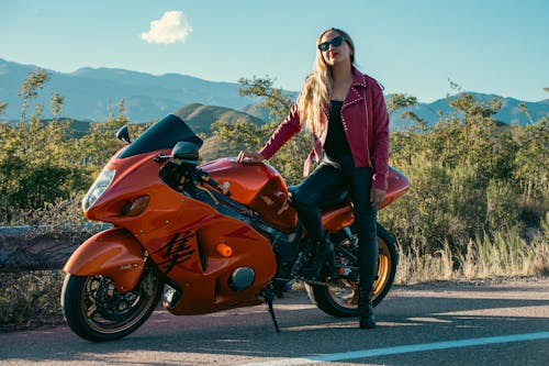 A woman in a red jacket is posing next to a motorcycle