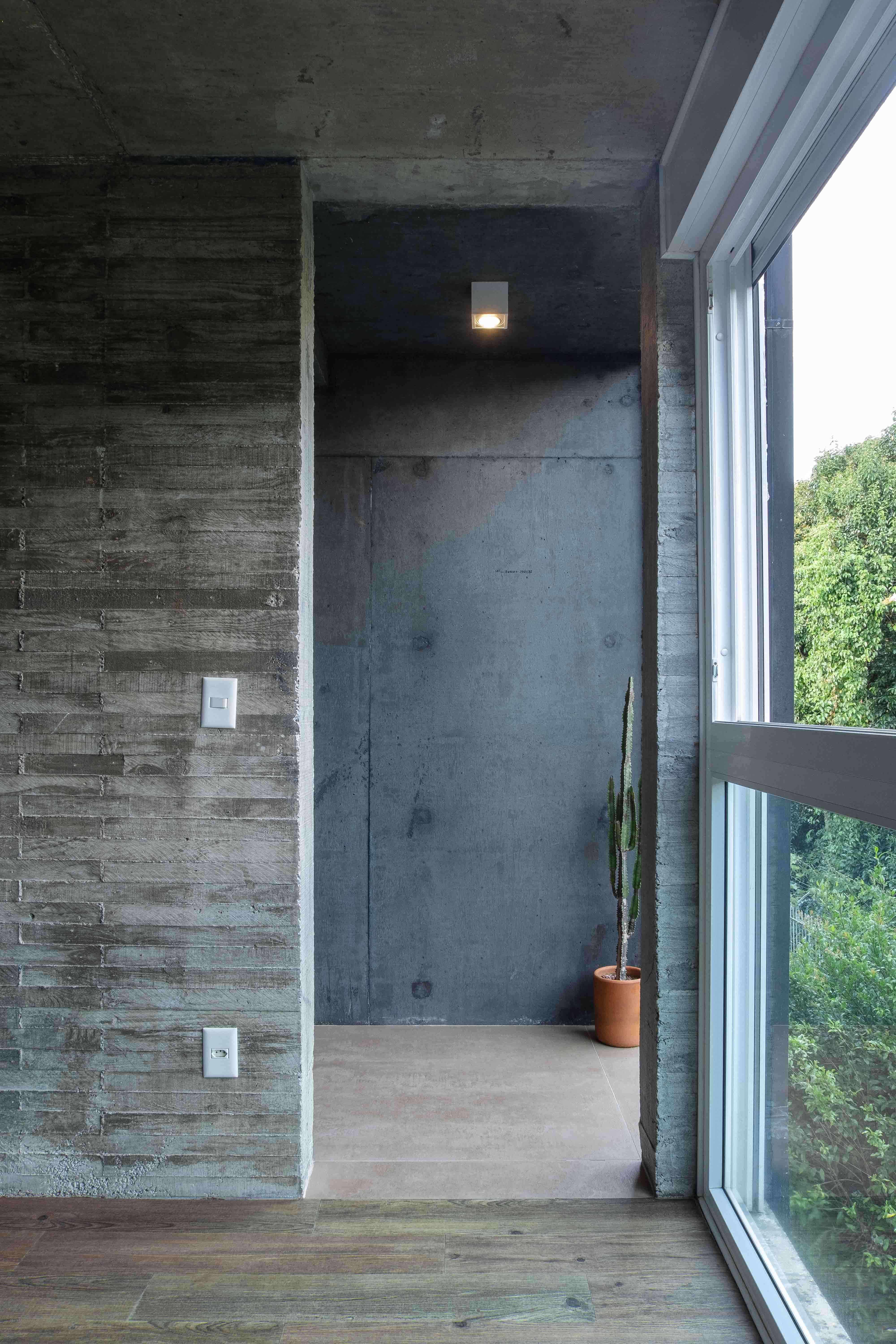 Minimalist indoor scene featuring concrete walls, large window, and potted plant.