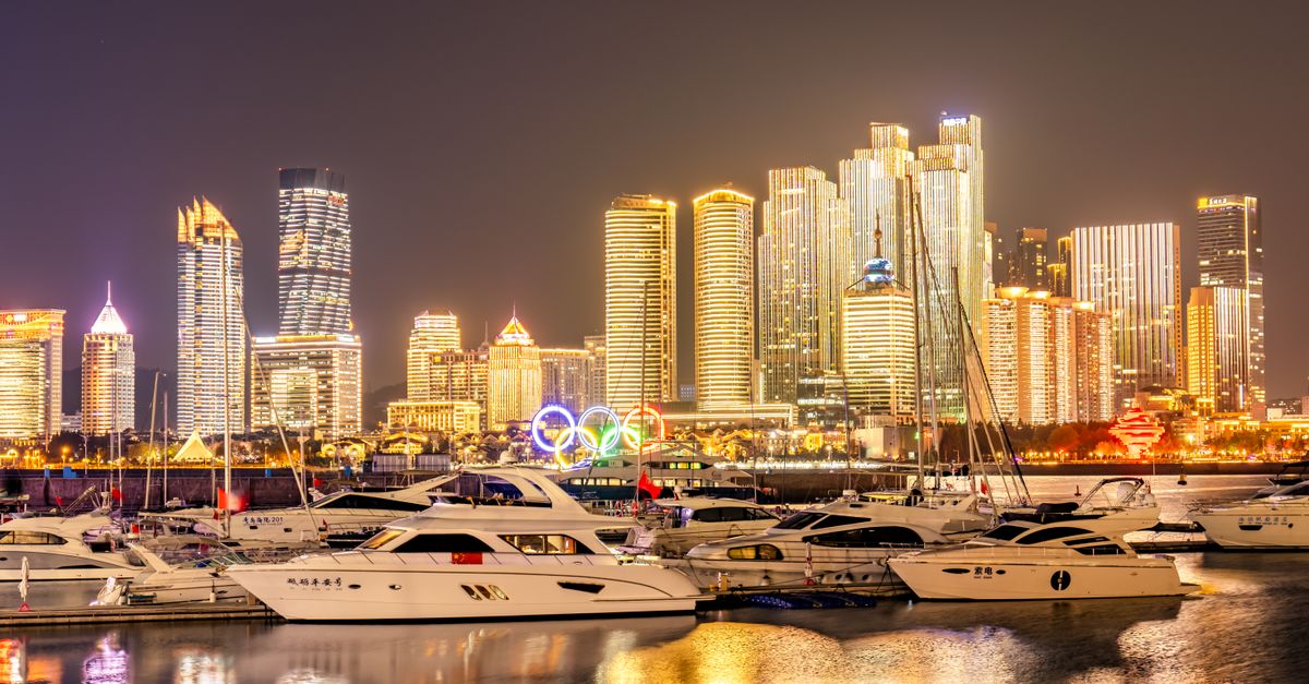 Qingdao's marina with motor yachts and glowing skyscrapers at night, showcasing its vibrant cityscape.