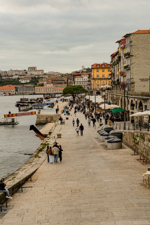 Free Explore the bustling riverside promenade in Porto, Portugal, packed with people, boats, and colorful architecture. Stock Photo