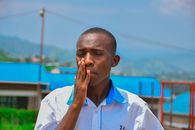 A thoughtful young man in a white shirt outdoors, set against a bright backdrop.