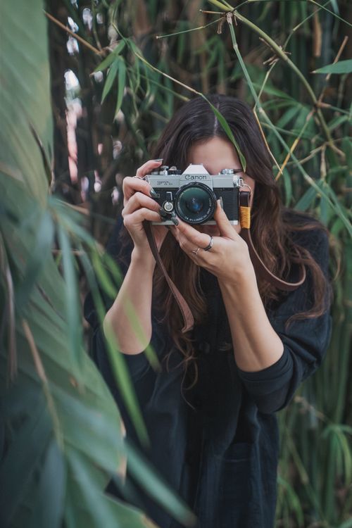 Free Young woman with long hair taking pictures with a vintage camera outdoors. Stock Photo