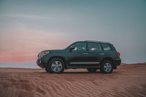 Free Side view of off-road SUV driving through desert dunes at twilight. Stock Photo