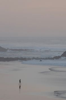 A solitary figure walks along a tranquil beach at twilight with gentle waves.
