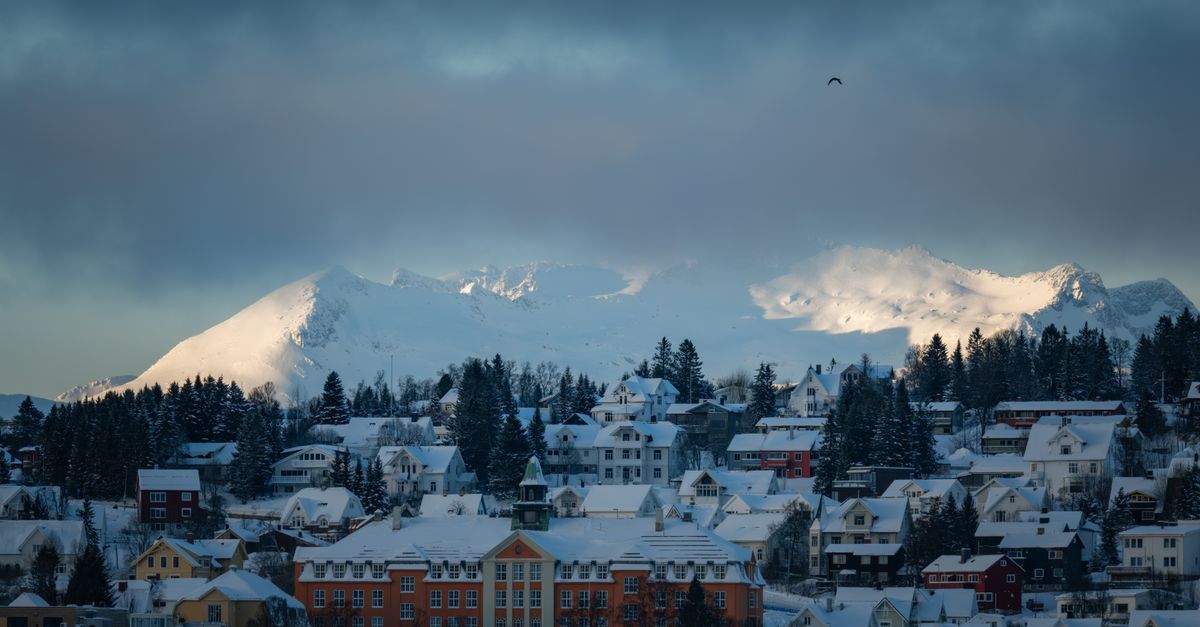 Picturesque snowy town against majestic mountains during winter dusk, showcasing urban tranquility.